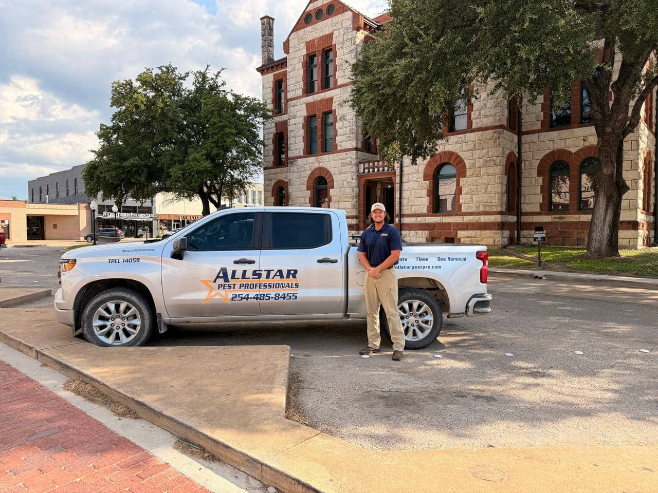 Allstar Pest Professionals technician standing beside a company pest control truck in front of a historic stone courthouse